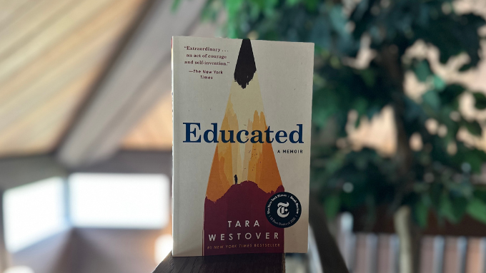 Educated (book) propped up on table with background of green tree and windows