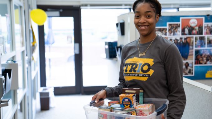 African American student wearing a TriO shirt and holding donations
