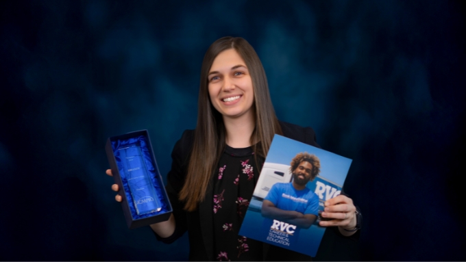 White woman with long straight brown hair holds a box that contains a glass award and a printed marketing handout