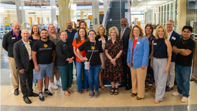 a diverse group of 18 adults stand together in the RVC library lobby