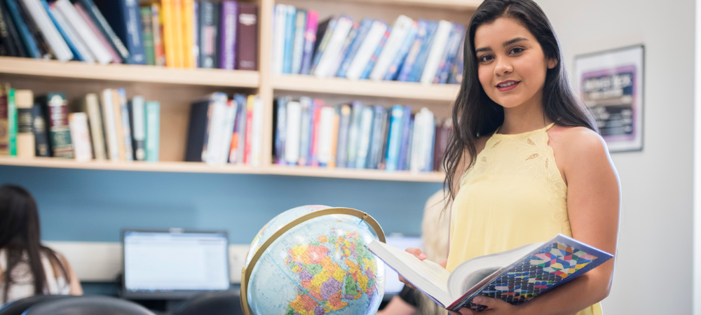 student holding open book standing next to globe