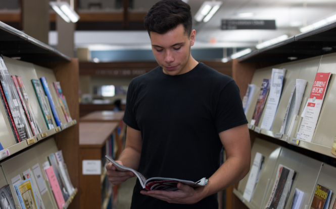 student in library holding magazine open student in library holding magazine open