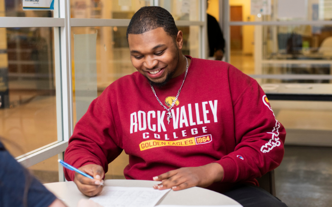 male student wearing red sweater writing in notebook