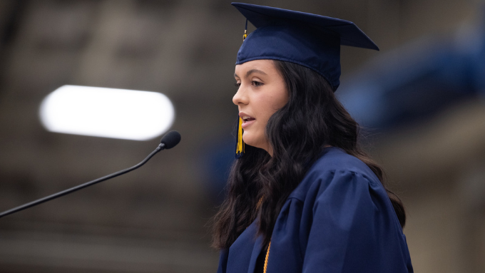 student commencement speaker Alyssa Bird wearing cap and gown at podium