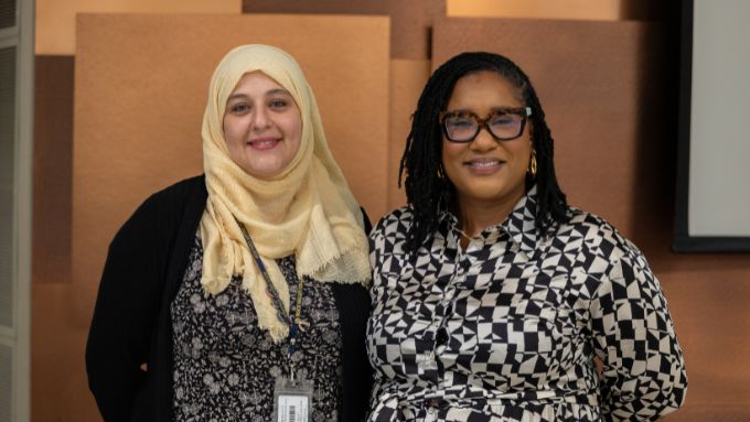Woman on left wearing an ivory hijab and African American woman on right wearing glasses and black and white checked shirt.