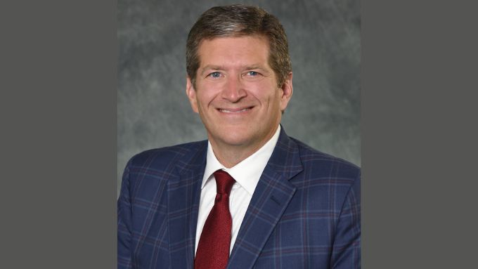 Middle aged white man in a blue plaid suit and red tie