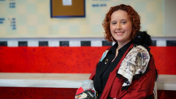 young white woman with shoulder length wavy red hair wears a black shirt and red satin gypsy robe