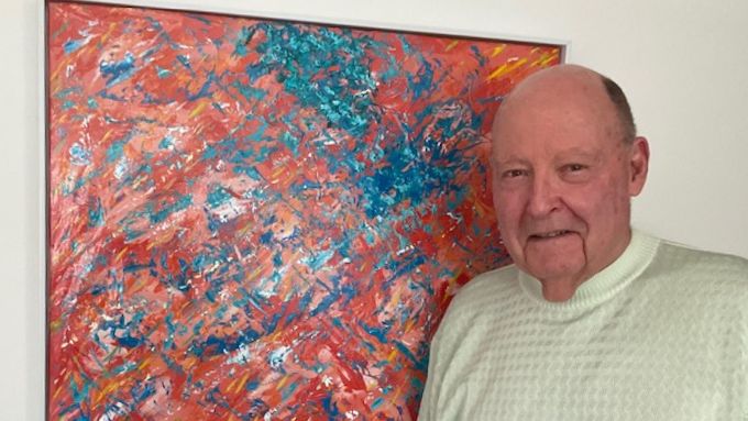 Older man standing next to his painting 