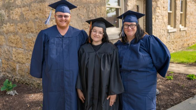 Three graduated wearing cap and gown; male left and two females on right