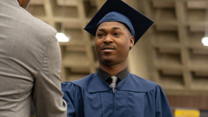 student wearing a cap and gown shaking a hand