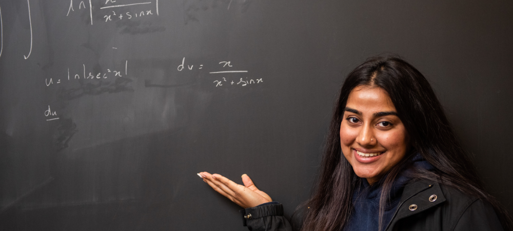 female student pointing hand to black chalkboard with math problem