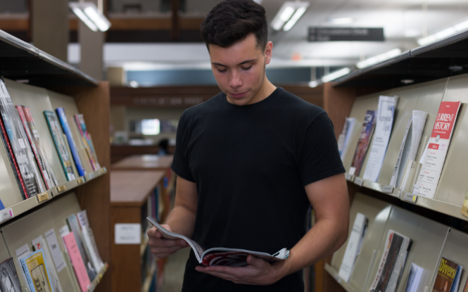 student in library holding magazine open
